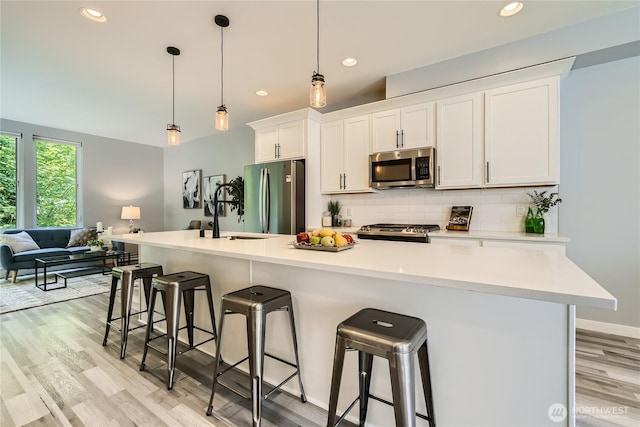 3540 S Graham St, Seattle, WA 98118 - kitchen featuring stainless steel appliances, a kitchen breakfast bar, light wood-style flooring, white cabinetry, and decorative backsplash