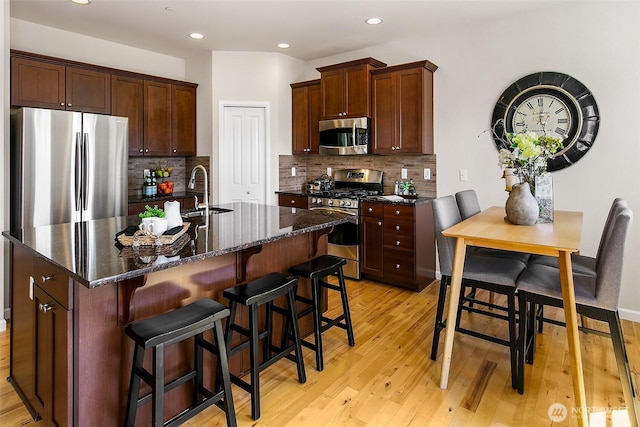 7649 NE 196th St, Kenmore, WA 98028 - kitchen featuring appliances with stainless steel finishes, light wood-style flooring, backsplash, a breakfast bar, and a kitchen island with sink