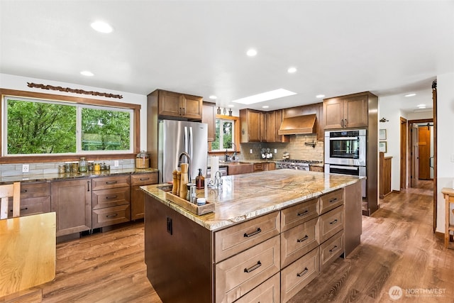 9317 214th Ave E, Bonney Lake, WA 98391 - kitchen featuring appliances with stainless steel finishes, custom exhaust hood, tasteful backsplash, a center island with sink, and recessed lighting
