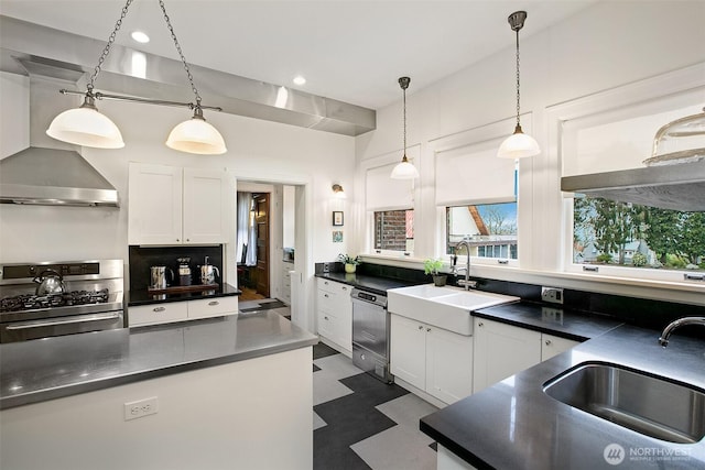 kitchen with stainless steel appliances, dark countertops, wall chimney exhaust hood, white cabinetry, and decorative light fixtures