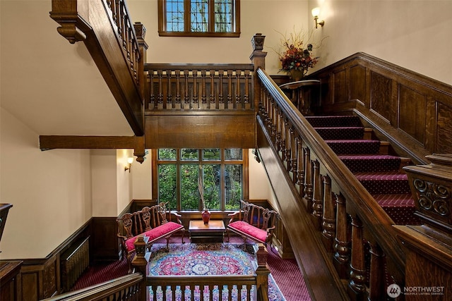 stairway with a towering ceiling, a wainscoted wall, and carpet