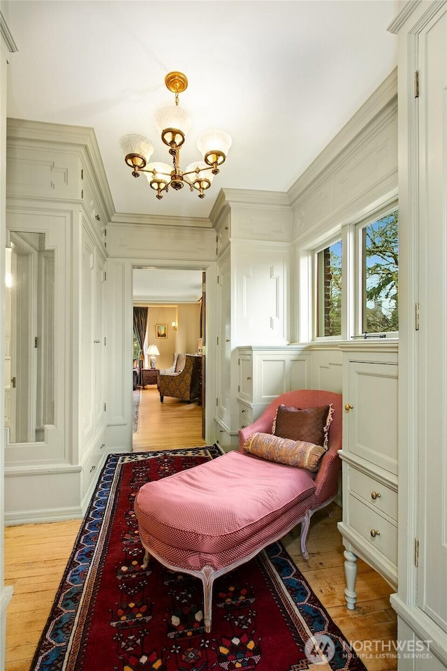 bedroom featuring light wood-style flooring, a chandelier, crown molding, and a decorative wall
