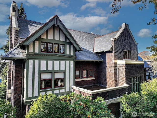 back of property with stucco siding, brick siding, a chimney, and a high end roof