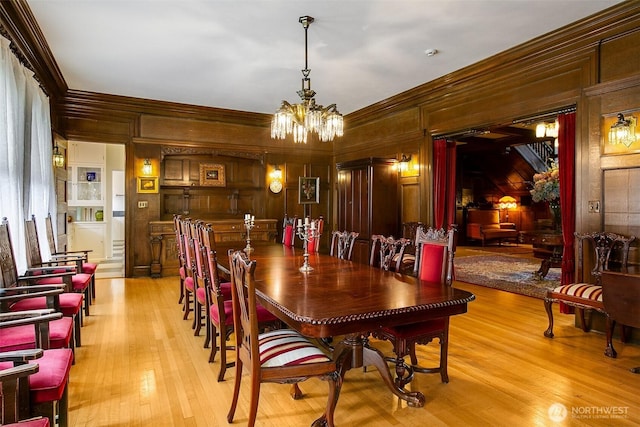dining area with ornamental molding, a chandelier, light wood-style flooring, and wooden walls