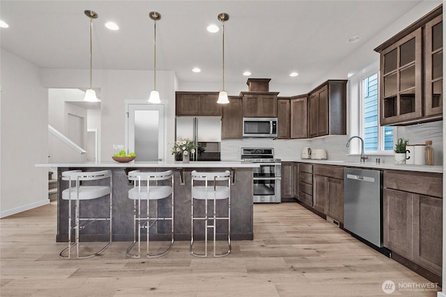 1401 89th Ave SE, Tumwater, WA 98501 - kitchen with appliances with stainless steel finishes, decorative backsplash, light wood-style flooring, dark brown cabinetry, and a breakfast bar