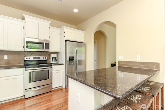 1605 Riddell Ave NE, Orting, WA 98360 - kitchen with appliances with stainless steel finishes, a peninsula, dark stone counters, white cabinets, and arched walkways