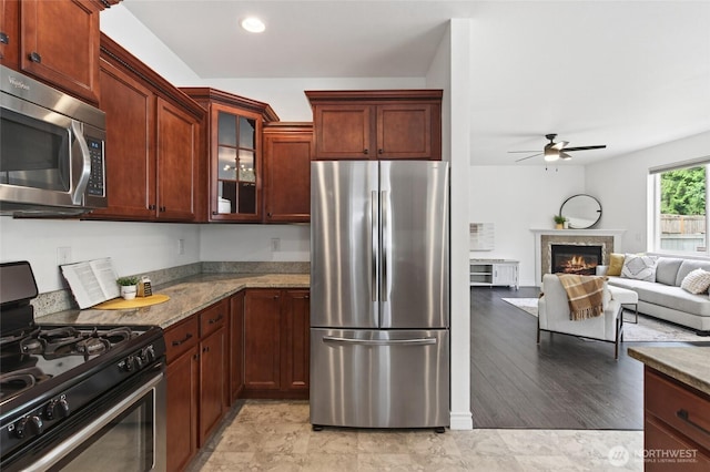 4246 Stonecrest Ct, Bellingham, WA 98226 - kitchen featuring appliances with stainless steel finishes, a ceiling fan, stone countertops, glass insert cabinets, and a premium fireplace