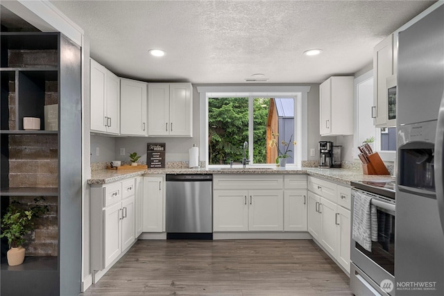 4415 Waller Rd E, Tacoma, WA 98443 - kitchen featuring stainless steel appliances, a textured ceiling, recessed lighting, white cabinets, and wood finished floors