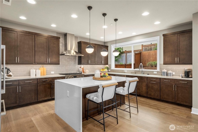 10259 133rd Ct NE, Redmond, WA 98033 - kitchen with wall chimney range hood, backsplash, light wood-type flooring, a breakfast bar, and dark brown cabinets