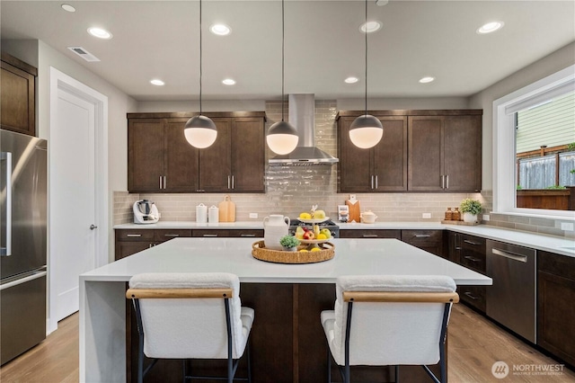 10259 133rd Ct NE, Redmond, WA 98033 - kitchen with appliances with stainless steel finishes, wall chimney range hood, light wood-style floors, light countertops, and a kitchen breakfast bar