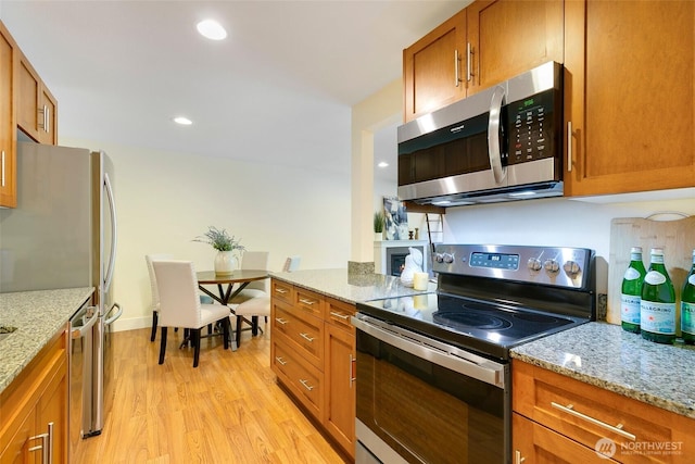 21307 48th Ave W Unit C211, Mountlake Terrace, WA 98043 - kitchen featuring stainless steel appliances, brown cabinets, light wood-style flooring, and light stone counters