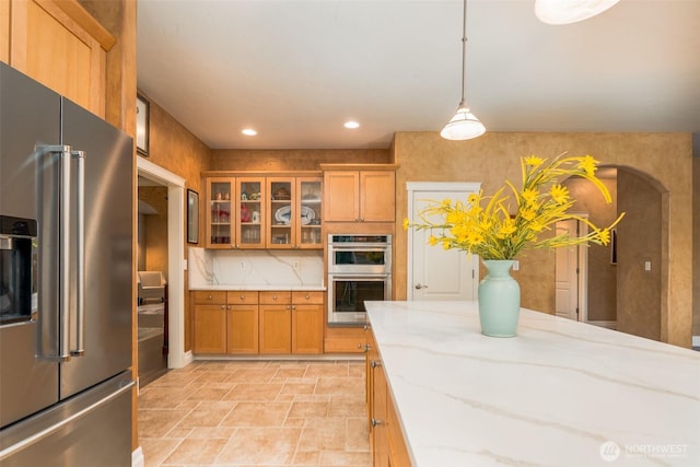 1122 36th Ave NE, Olympia, WA 98506 - kitchen featuring appliances with stainless steel finishes, brown cabinets, glass insert cabinets, light stone countertops, and stone finish floors