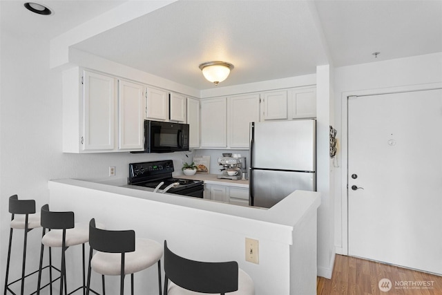 2727 E Franklin Ave E Unit 102, Seattle, WA 98102 - kitchen featuring black appliances, a peninsula, white cabinetry, a kitchen breakfast bar, and light countertops