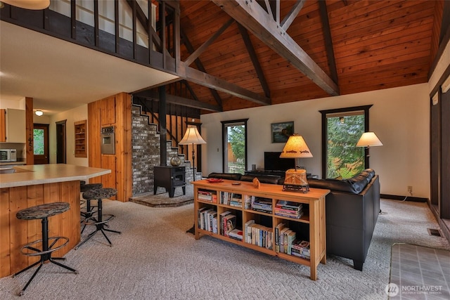 24302 Saddle St, Leavenworth, WA 98826 - living room featuring light colored carpet, a wooden ceiling with exposed beams, a wood stove, high vaulted ceiling, and wood walls