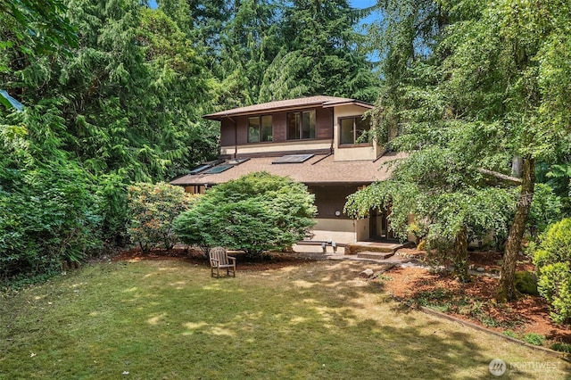 back of house featuring a lawn and a shingled roof