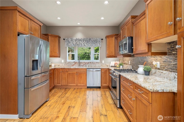 4119 72nd St E, Tacoma, WA 98443 - kitchen with stainless steel appliances, brown cabinets, light wood-type flooring, light stone countertops, and backsplash