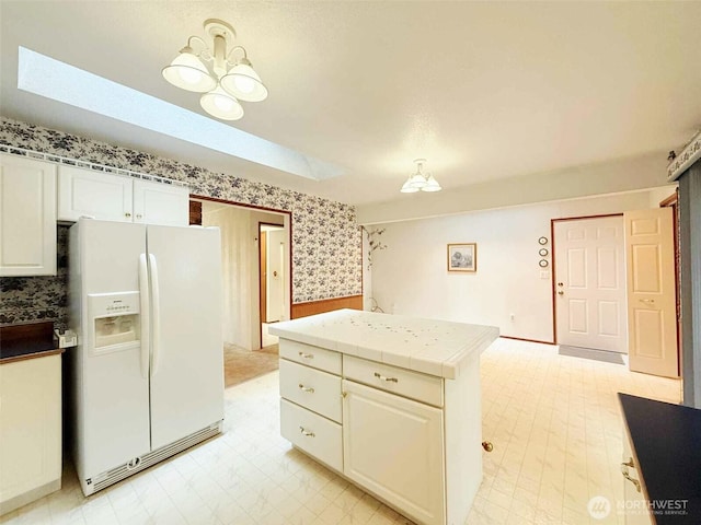 4905 US Highway 12, Elma, WA 98541 - kitchen featuring white fridge with ice dispenser, wallpapered walls, wainscoting, tile countertops, and white cabinets
