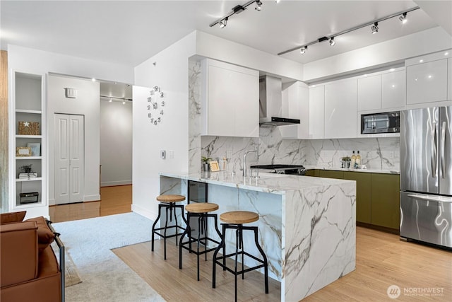 7800 SE 27th St Unit 302, Mercer Island, WA 98040 - kitchen with appliances with stainless steel finishes, wall chimney exhaust hood, modern cabinets, a kitchen bar, and white cabinetry