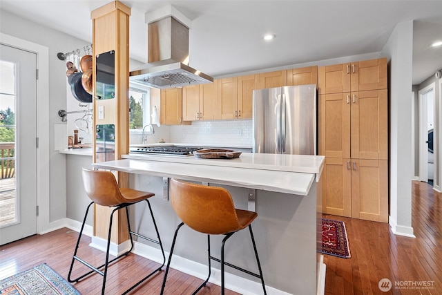 6511 Canyon Ct SW, Olympia, WA 98512 - kitchen featuring appliances with stainless steel finishes, island exhaust hood, light brown cabinetry, a breakfast bar, and recessed lighting