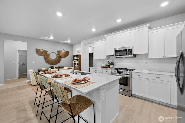 14121 195th Street Ct E, Graham, WA 98338 - kitchen with appliances with stainless steel finishes, a kitchen island with sink, light countertops, light wood finished floors, and recessed lighting