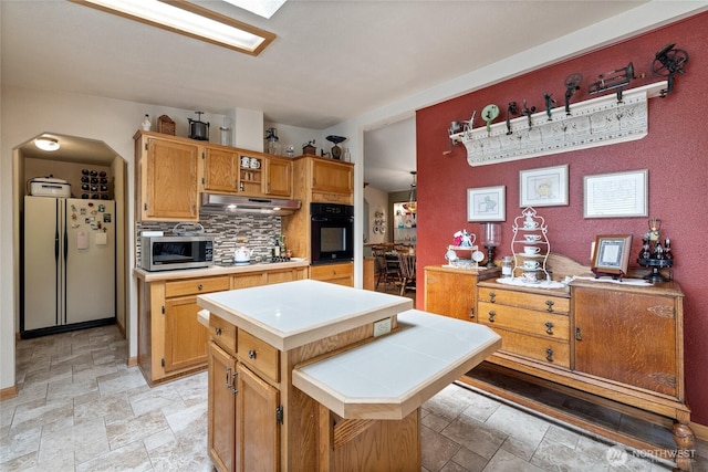 836 Harman Way S Unit 82, Orting, WA 98360 - kitchen with appliances with stainless steel finishes, under cabinet range hood, stone finish flooring, tasteful backsplash, and tile countertops