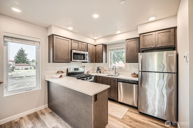 1823 SW 96th Ln, Seattle, WA 98106 - kitchen featuring stainless steel appliances, dark brown cabinetry, a peninsula, light countertops, and light wood finished floors