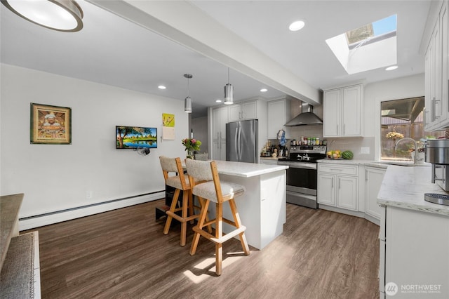 7818 185th Pl SW, Edmonds, WA 98026 - kitchen with appliances with stainless steel finishes, a baseboard radiator, wall chimney exhaust hood, wood finished floors, and a kitchen bar