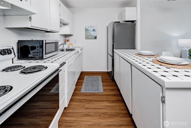 303 N 44th St Unit 105, Seattle, WA 98103 - kitchen featuring appliances with stainless steel finishes, exhaust hood, white cabinets, tile countertops, and wood finished floors