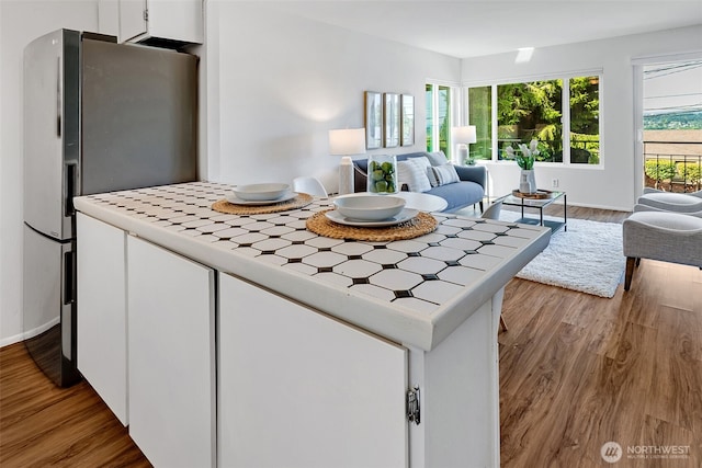 303 N 44th St Unit 105, Seattle, WA 98103 - kitchen featuring tile counters, freestanding refrigerator, white cabinets, wood finished floors, and open floor plan