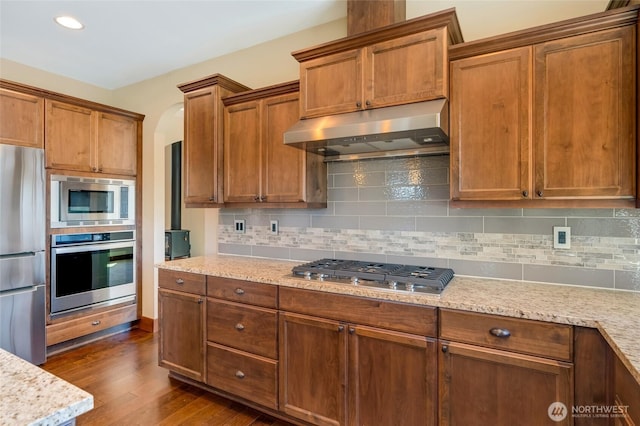 5728 SE 159th Ave, Snohomish, WA 98290 - kitchen with stainless steel appliances, under cabinet range hood, backsplash, dark wood-style flooring, and brown cabinetry