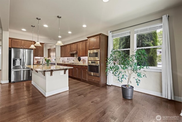 8910 Buttercup St SE, Tumwater, WA 98501 - kitchen featuring stainless steel appliances, light stone countertops, a kitchen bar, recessed lighting, and under cabinet range hood