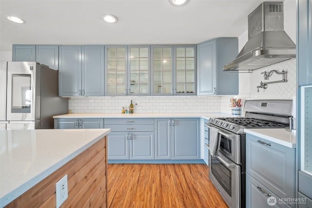 6084 Summit View Pl, Ferndale, WA 98248 - kitchen with wall chimney range hood, stainless steel appliances, light countertops, light wood-type flooring, and glass insert cabinets