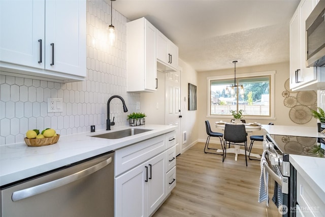 1626 E 59th St, Tacoma, WA 98404 - kitchen featuring appliances with stainless steel finishes, decorative backsplash, white cabinetry, pendant lighting, and light wood-style flooring