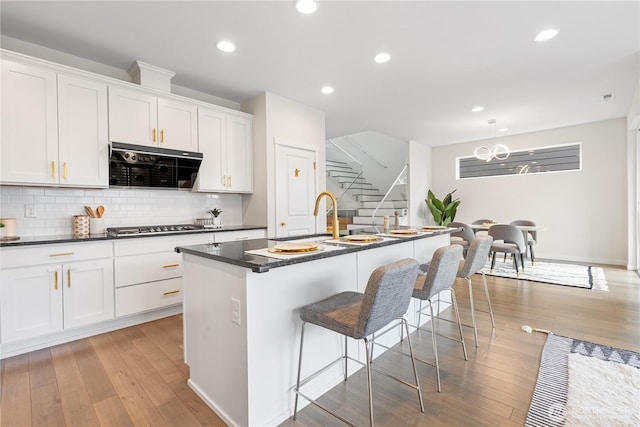 23228 SE 50th St, Issaquah, WA 98029 - kitchen with dark countertops, light wood-style floors, a kitchen island with sink, stainless steel gas stovetop, and recessed lighting