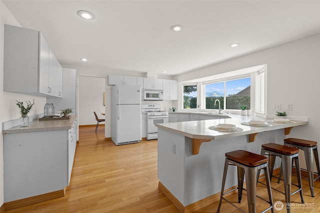 15120 61st St E, Sumner, WA 98390 - kitchen featuring white appliances, a peninsula, a breakfast bar, light wood-style floors, and white cabinetry