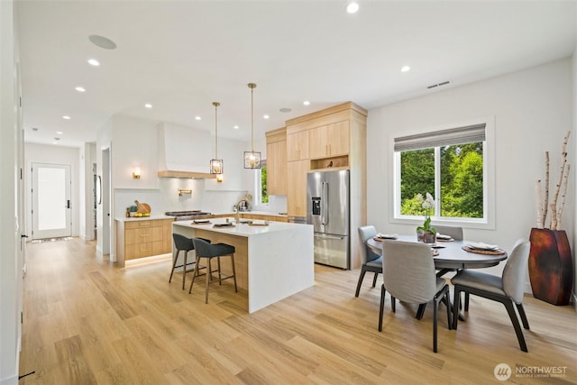 9051 Sea Mist Ln, Blaine, WA 98230 - kitchen with stainless steel fridge with ice dispenser, light brown cabinets, modern cabinets, custom range hood, and light wood-type flooring