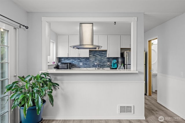 12240 SE 60th St Unit 41, Bellevue, WA 98006 - kitchen featuring wall chimney range hood, stainless steel appliances, tasteful backsplash, white cabinetry, and wood finished floors