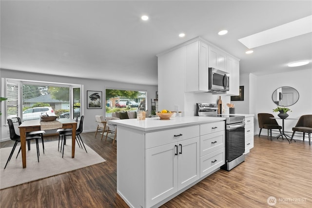 7411 201st St SW, Lynnwood, WA 98036 - kitchen with stainless steel appliances, a skylight, dark wood-type flooring, white cabinets, and light countertops