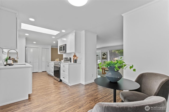 7411 201st St SW, Lynnwood, WA 98036 - kitchen featuring stainless steel appliances, a skylight, white cabinetry, light wood-style floors, and recessed lighting