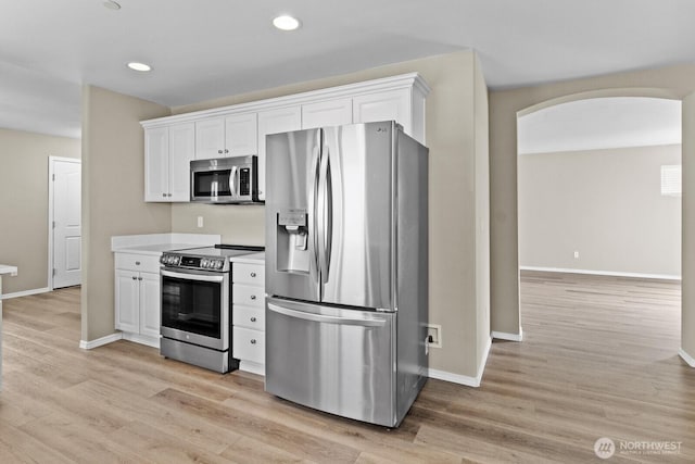 2237 Tolmie St, Dupont, WA 98327 - kitchen with stainless steel appliances, arched walkways, white cabinetry, light wood-type flooring, and recessed lighting