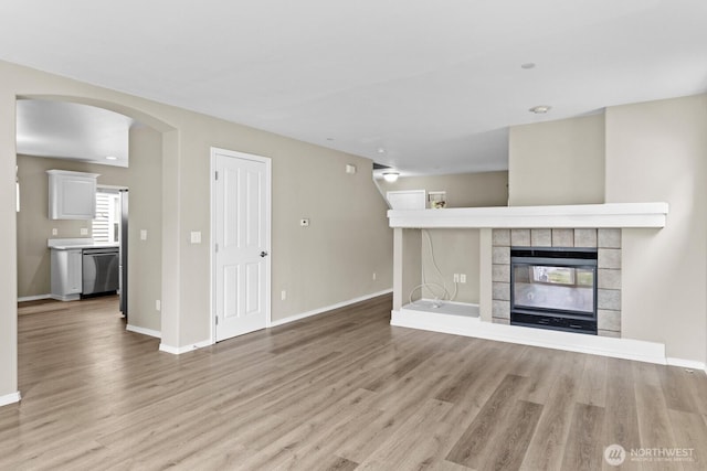 2237 Tolmie St, Dupont, WA 98327 - unfurnished living room featuring light wood finished floors, a tiled fireplace, and arched walkways