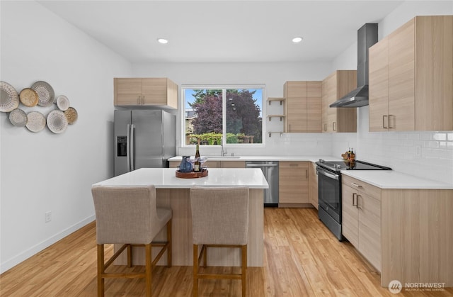 9228 21st Ave SW, Seattle, WA 98106 - kitchen with appliances with stainless steel finishes, wall chimney range hood, light brown cabinets, a breakfast bar area, and modern cabinets
