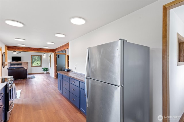13402 Spring Site Rd E, Orting, WA 98360 - kitchen with appliances with stainless steel finishes, blue cabinets, light wood-type flooring, a brick fireplace, and open floor plan