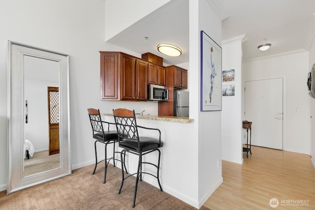 225 Logan Ave S Unit B355, Renton, WA 98057 - kitchen featuring appliances with stainless steel finishes, a kitchen bar, ornamental molding, brown cabinets, and light wood-style floors