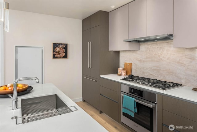 2510 6th Ave Unit 3605, Seattle, WA 98121 - kitchen featuring appliances with stainless steel finishes, under cabinet range hood, backsplash, light wood-style flooring, and light countertops