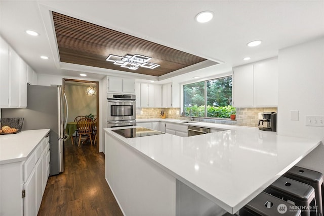 13222 76th Avenue Ct E, Puyallup, WA 98373 - kitchen with a peninsula, a tray ceiling, tasteful backsplash, recessed lighting, and dark wood-style flooring