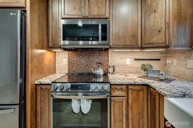 1732 NW 29th Cir, Camas, WA 98607 - kitchen with appliances with stainless steel finishes, backsplash, light stone counters, and brown cabinetry