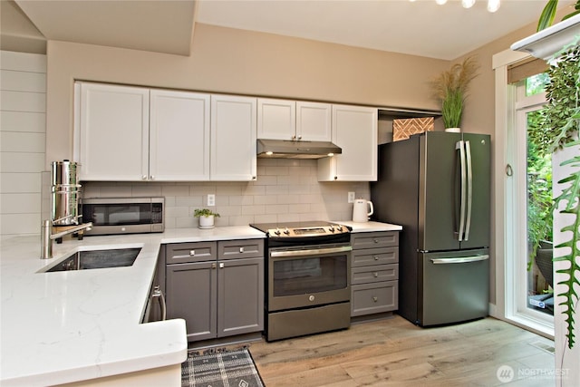 23300 SE Black Nugget Rd Unit J3, Issaquah, WA 98029 - kitchen with appliances with stainless steel finishes, under cabinet range hood, decorative backsplash, light stone countertops, and light wood-type flooring