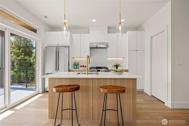 6732 21st Ave SW, Seattle, WA 98106 - kitchen with range hood, light countertops, white cabinets, a center island with sink, and a kitchen breakfast bar