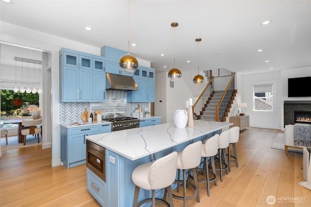 6209 32nd Ave NE, Seattle, WA 98115 - kitchen featuring appliances with stainless steel finishes, under cabinet range hood, blue cabinets, light wood-style flooring, and recessed lighting